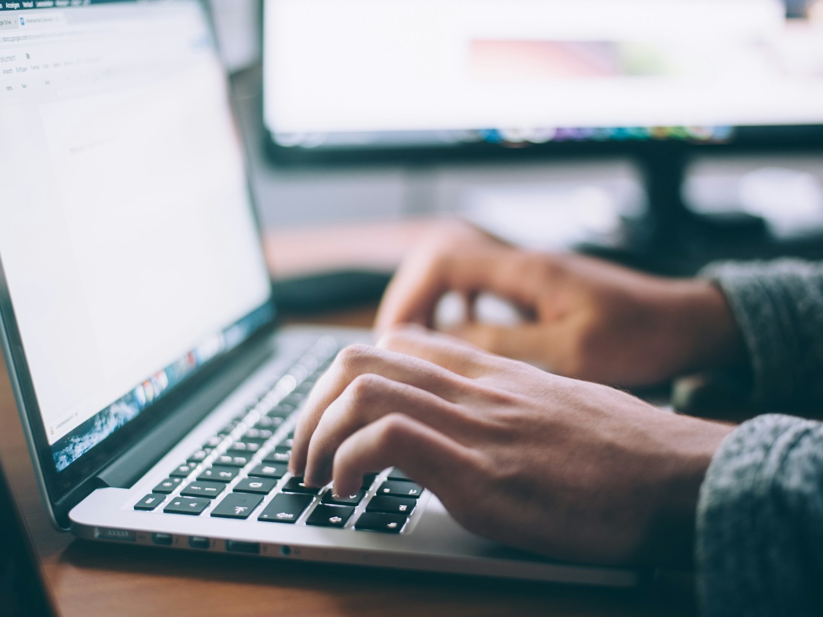An open laptop on a white desk beside a plant.