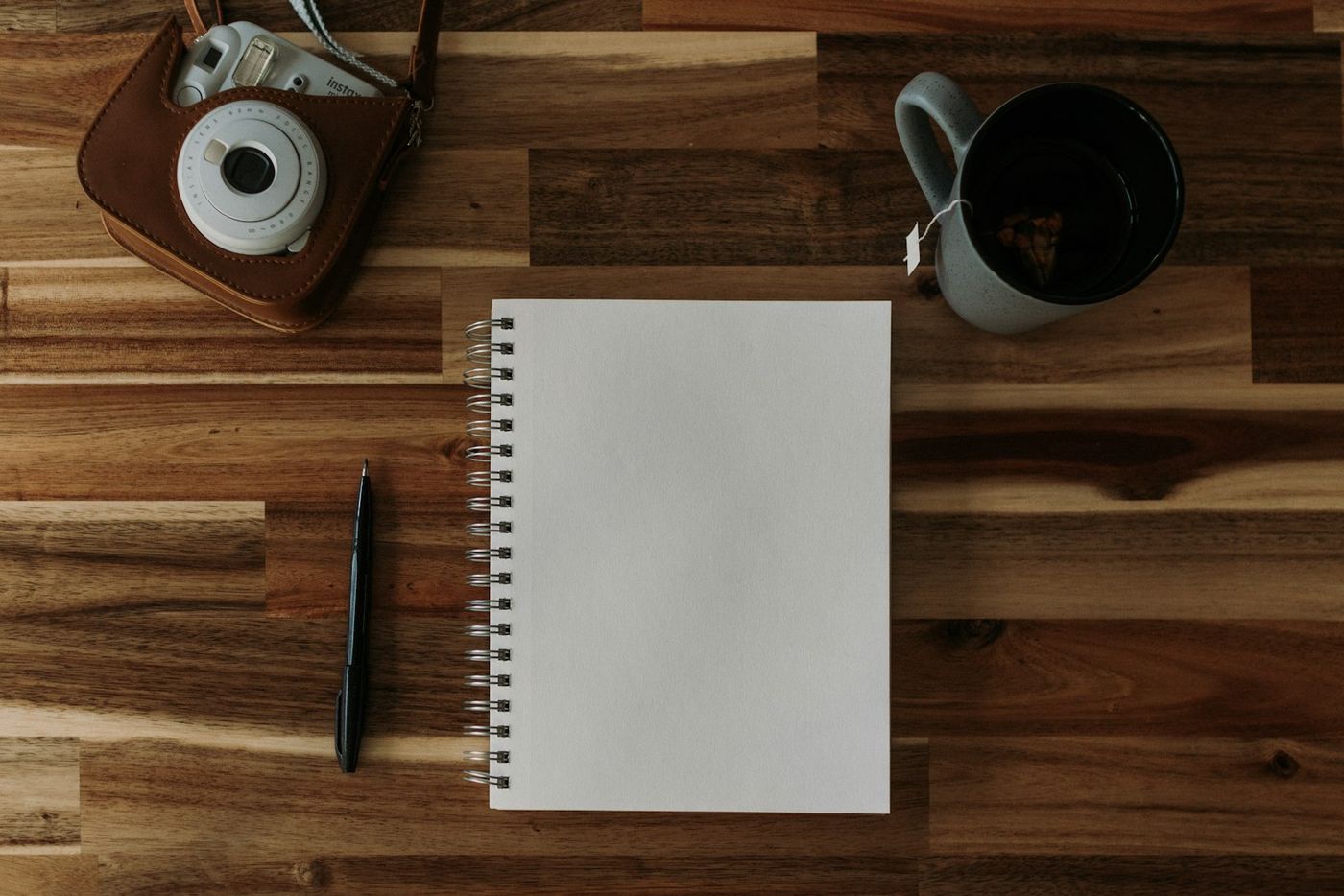 Notepad, pen, vintage camera and a cup of coffee on a wooden table