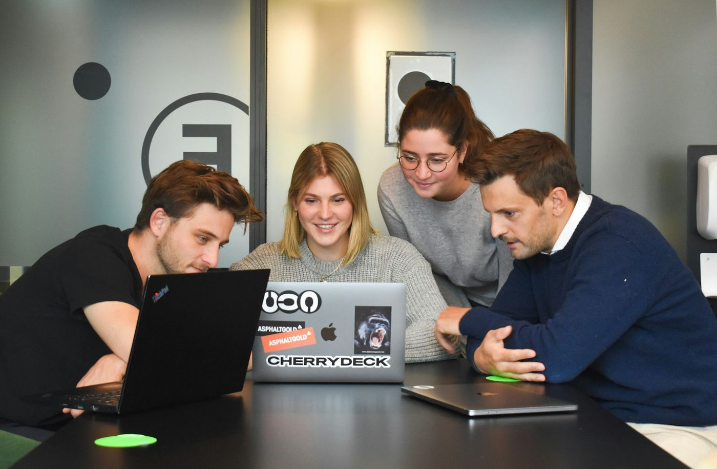 Four colleagues gathered around a laptop at a table in a bright office