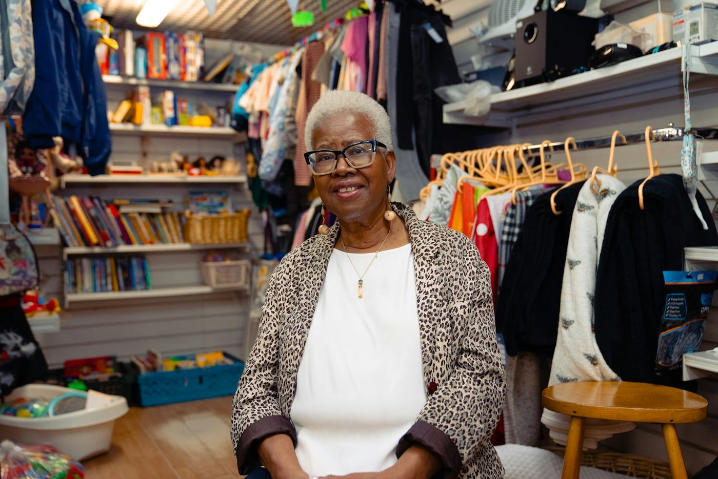Smiling older woman standing in a small clothing shop with racks and shelves behind her